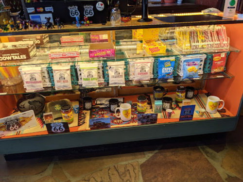 A display case filled with souvenirs, snacks, and mugs, featuring Route 66 memorabilia and colorful packaging.